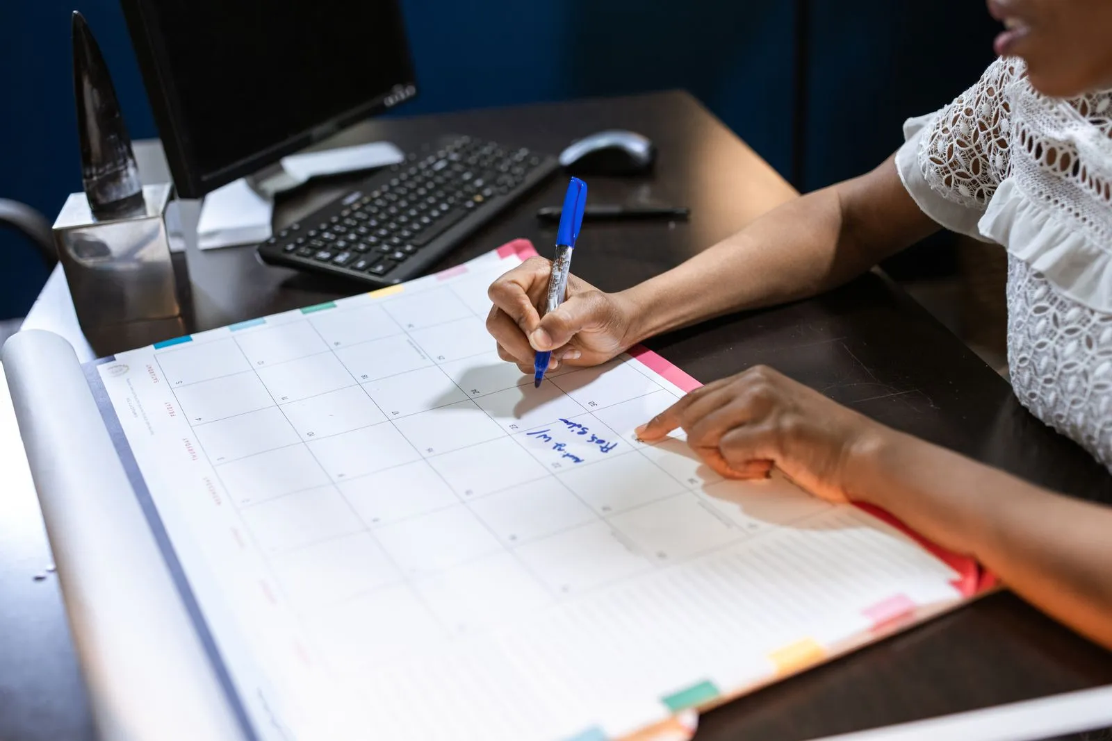 A person marking a pay date on a wall calendar with a marker